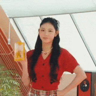 a woman in a red shirt and plaid skirt is holding a box of banana juice .