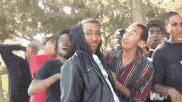 a group of young men are standing in a park . one of the men is wearing a hoodie .
