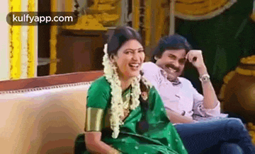 a man and a woman are sitting on a couch and laughing together .