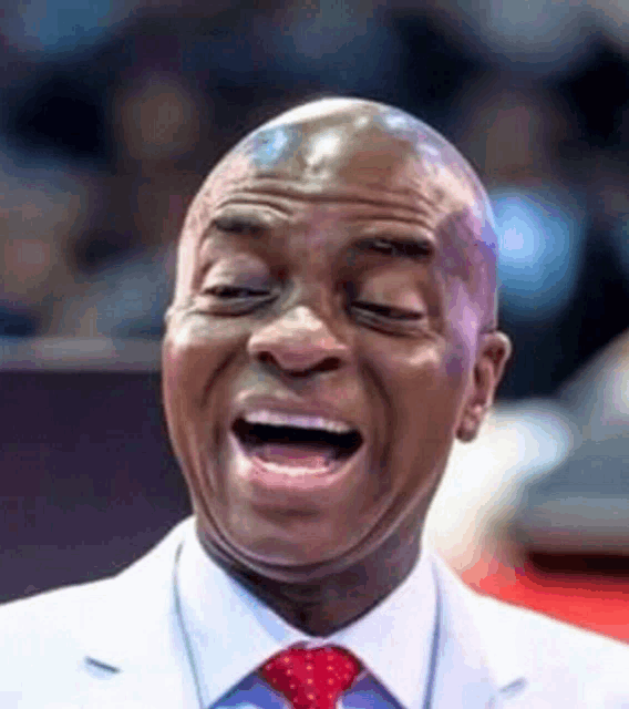 a man in a white suit and red tie is making a funny face with his mouth open .