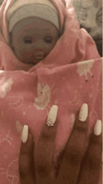 a doll wrapped in a pink blanket is being held by a woman with white nails