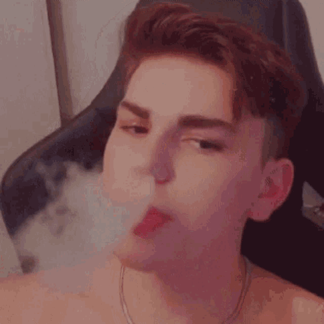 a young man is sitting in a chair smoking a cigarette .