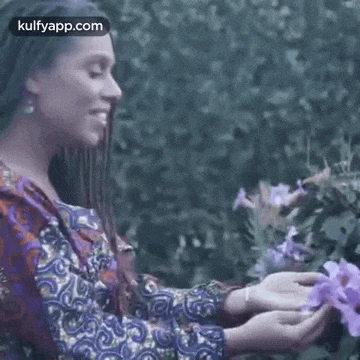 a woman with braids is smelling a purple flower .