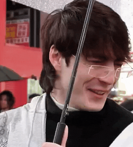 a young man wearing glasses is holding an umbrella in his hand .