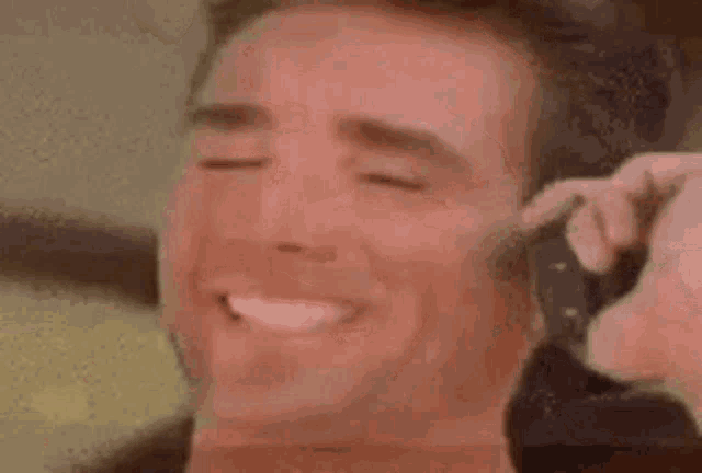 a close up of a man 's face with his eyes closed and a person holding a gun behind his ear .