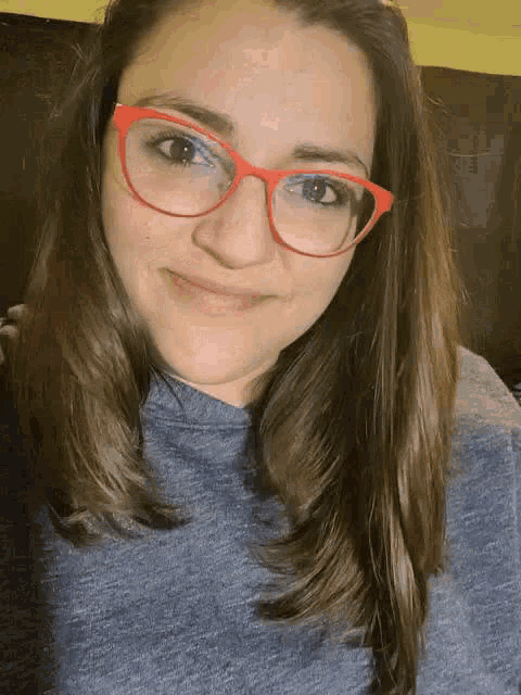 a woman wearing red glasses and a grey sweater is smiling .