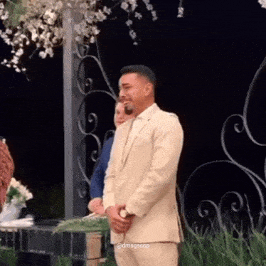 a man in a tan suit is standing in front of a bride and groom at a wedding .