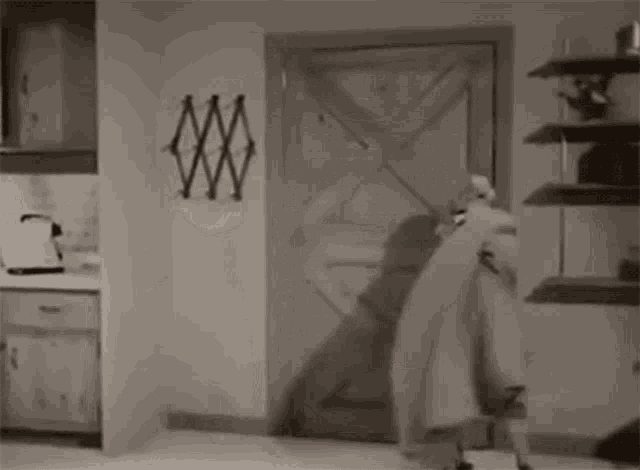 a black and white photo of a man standing in a doorway in a room .
