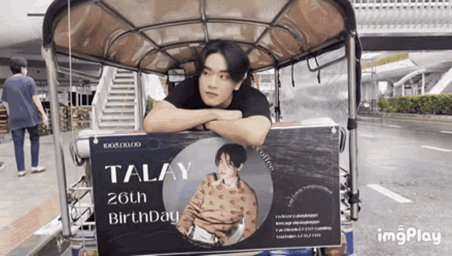 a man leaning on a sign that says talay on it
