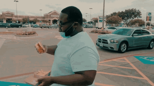 a man eating a hamburger in a parking lot with a kroger store in the background