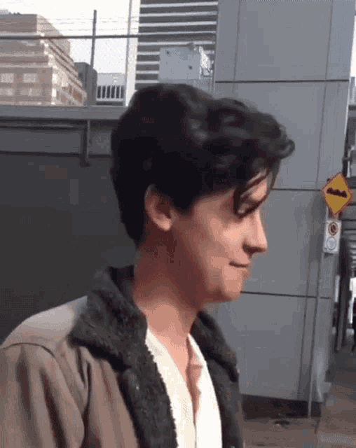 a young man wearing a jacket and a white shirt is walking down a sidewalk .