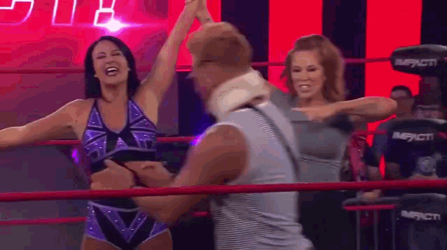 two women are wrestling in a ring and one of them is holding a man 's head .