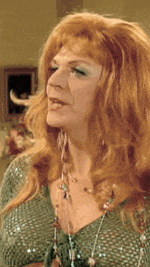 a woman with red hair and green eye shadow is wearing a green top