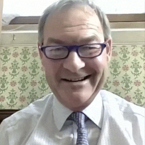 a man wearing glasses and a tie is smiling in front of a wall with flowers on it