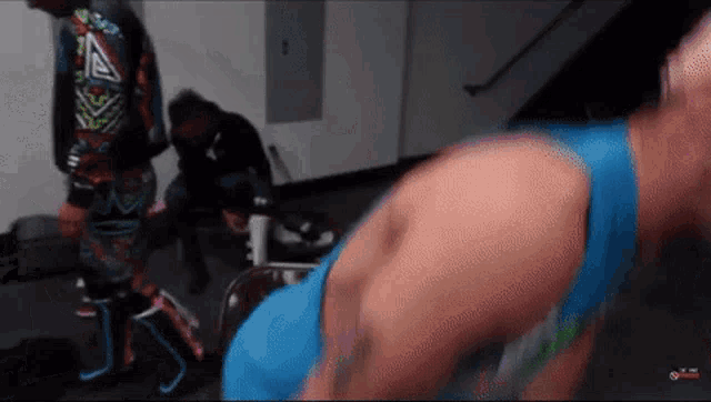 a man in a blue tank top is doing push ups in a gym while another man watches .