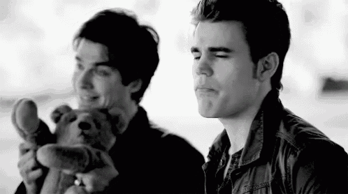 two men are sitting next to each other holding teddy bears and smiling .