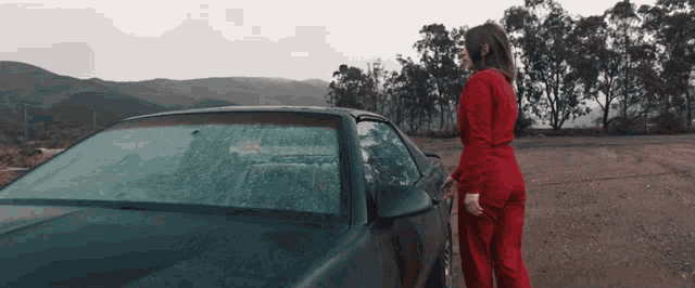 a woman in red standing next to a car