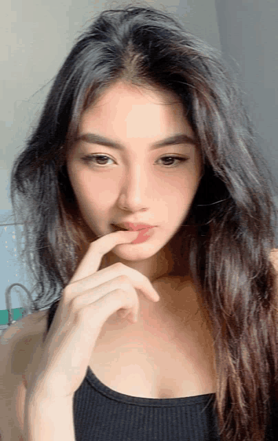 a woman in a black tank top has her finger on her mouth