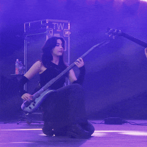 a woman playing a guitar in front of a purple sign that says tw
