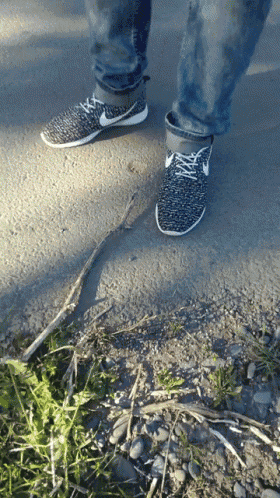 a person wearing a pair of nike shoes standing on a gravel road