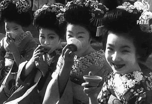 a black and white photo of a group of geishas drinking tea from cups .