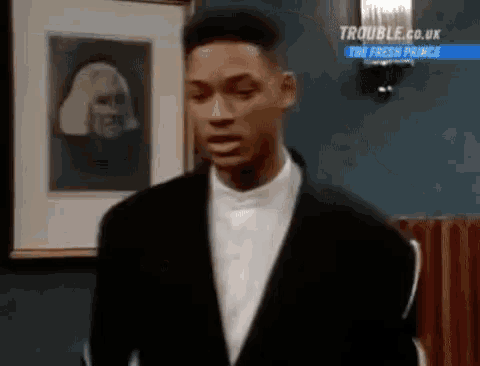 a man in a suit and white shirt is standing in front of a framed picture of a woman .