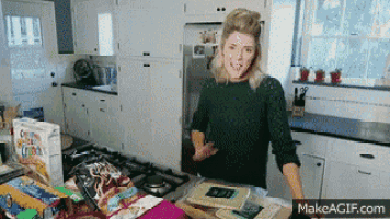 a woman standing in a kitchen with a box of cereal in front of her