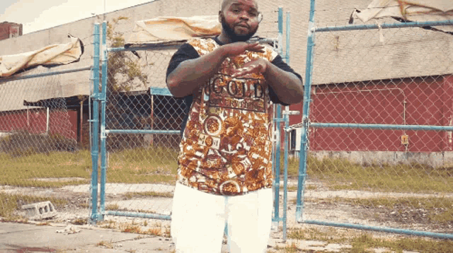 a man standing in front of a chain link fence wearing a gold shirt