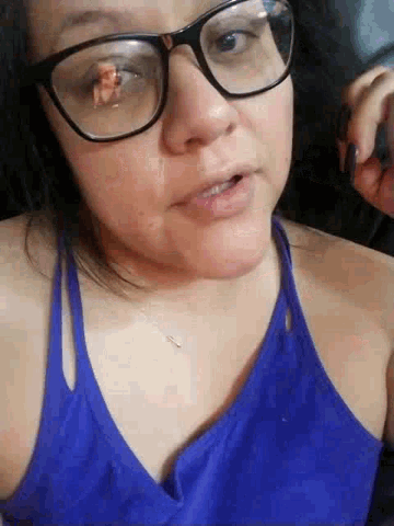 a woman wearing glasses and a blue tank top is smiling .