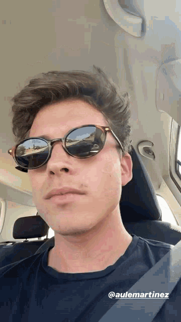 a man wearing sunglasses is sitting in a car with the name @aulemartinez on the bottom right
