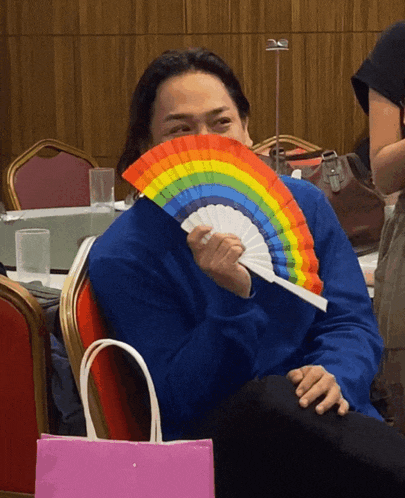 a man in a blue shirt is holding a rainbow fan