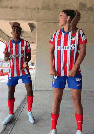 two female soccer players wearing red white and blue striped jerseys with herbalife on them