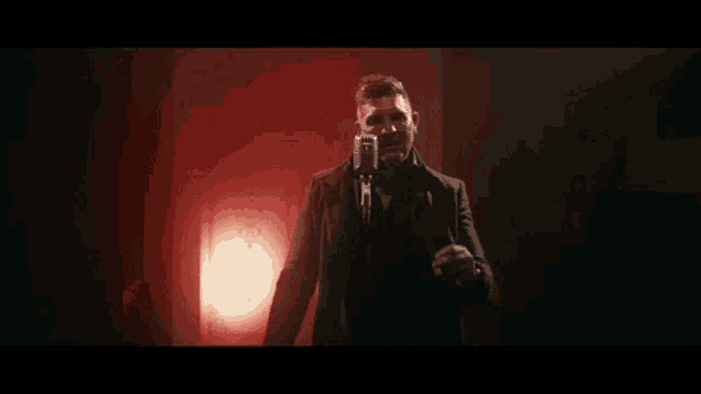 a man is singing into a microphone in a dark room with red lights .