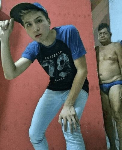 a boy wearing a republic 79 shirt stands in front of a man in blue underwear