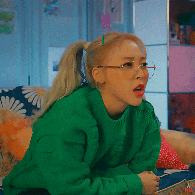 a woman wearing a green sweater and glasses is sitting on a couch