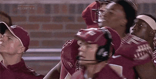 a group of football players are standing in a huddle with a coach wearing a headset .