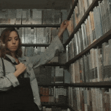a woman reaches for a book in a library with a book that says ' cine ' on the spine