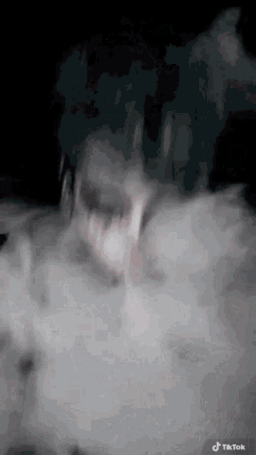 a person with blue hair is smoking a cigarette and smoke is coming out of their mouth .