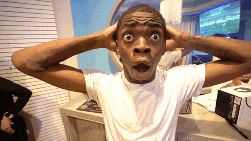 a man in a white shirt has his mouth open and his hands on his ears