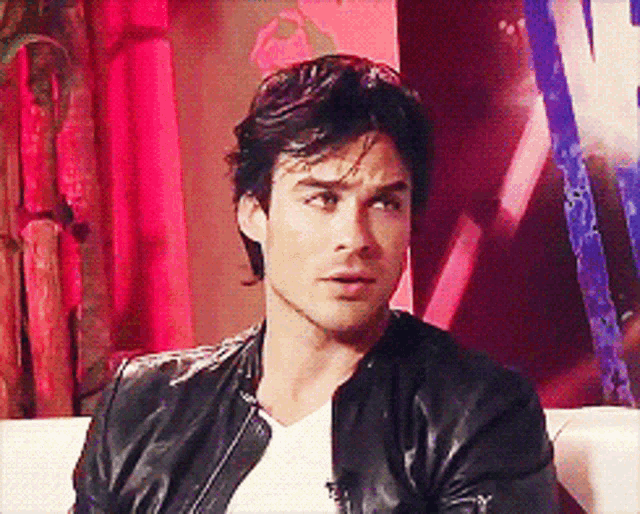 a man in a black leather jacket is sitting on a white couch