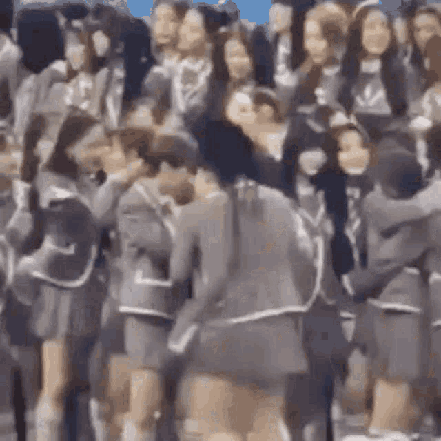 a group of people in school uniforms are kissing in front of a crowd of people .