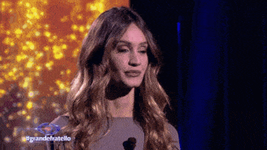 a woman stands on a stage in front of a blue curtain with the words grandefratello on it