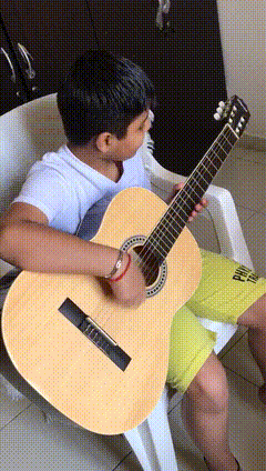 a young boy is playing an acoustic guitar while sitting in a white chair