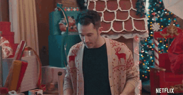 a man is standing in front of a gingerbread house and a christmas tree .