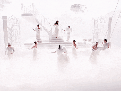 a group of people in white dresses are dancing in a foggy room