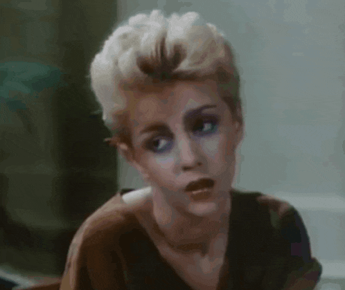 a woman with short blonde hair and blue eyes is making a funny face in a close up of her face .