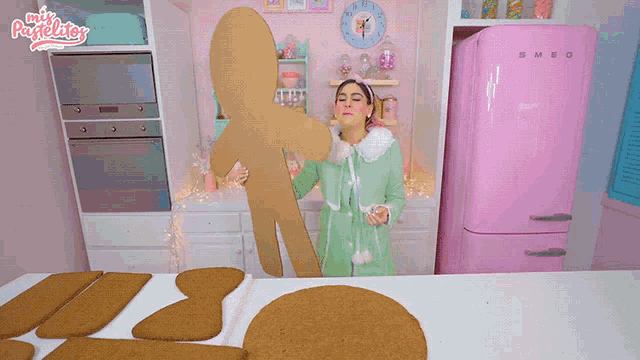 a pink smeg refrigerator sits in a kitchen next to a gingerbread man cut out of cardboard