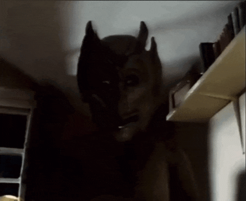 a statue of a demon with horns is standing in a dark room next to a shelf .
