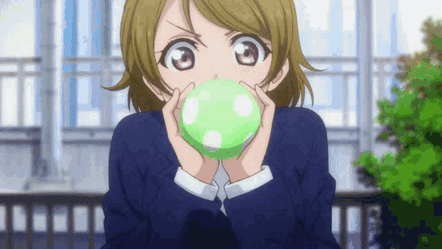 a girl in a school uniform blowing up a green balloon