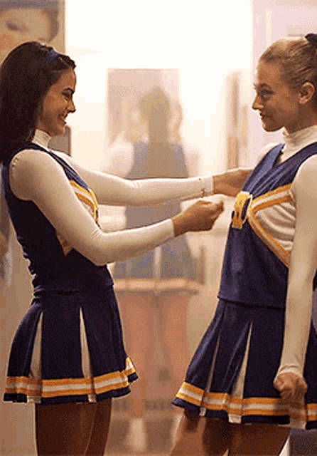 two cheerleaders are standing next to each other and one of them is wearing a uniform with the letter v on it .
